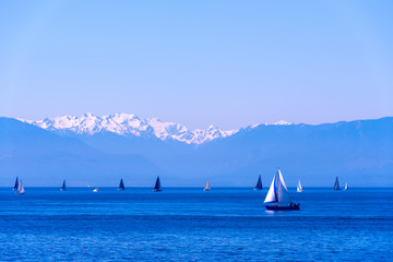 Sailboats and view of Olympic Mountains covered with snow on clear beautiful day during summer,...