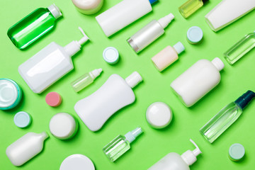 Top view of different cosmetic bottles and container for cosmetics on green background. Flat lay composition with copy space