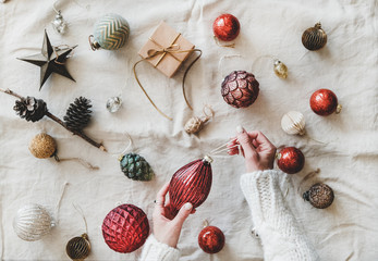 Christmas or New Year background, texture, wallpaper. Flat-lay of Christmas festive decoration toys and woman's hands in sweater over beige linen cloth, top view. Preparation for winter holiday season