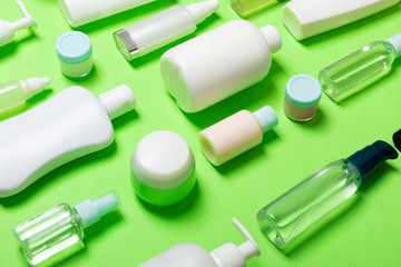 Close-up set of diffrent sized bottles and jars for cosmetic products on green backgound. Face and body care concept with copy space