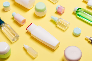 Composition of different sized cosmetic jars and bottles on yellow background. Beauty care concept with copy space