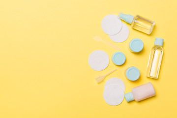 Group of small bottles for travelling on yellow background. Copy space for your ideas. Flat lay composition of cosmetic products. Top view of cream containers with cotton pads