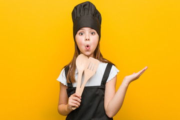 Little caucasian girl wearing a chef costume impressed holding copy space on palm.