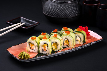Close up rainbow Sushi Roll with salmon, eel, tuna, avocado, royal prawn, cream cheese Philadelphia, caviar tobica, chuka. Sushi menu. Japanese food and green tea teapot, copyspace.
