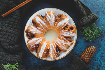 Creative flat lay, top view of Swedish tea ring Christmas cake with cinnamon, pecans and raisins on a warm knitted sweater. The concept of cozy winter Holidays and homemade bakery.