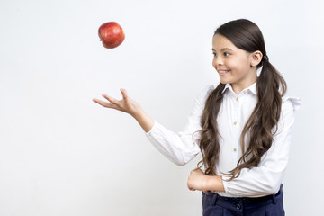 Playful Hispanic schoolgirl tossing apple