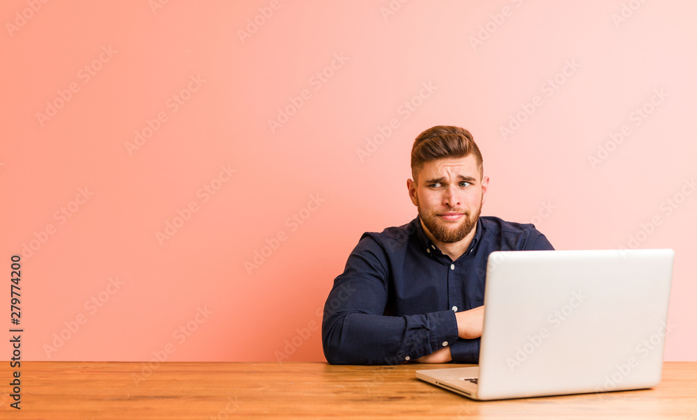 Wall mural Young man working with his laptop confused, feels doubtful and unsure. - Wall murals