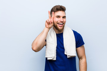 Young caucasian sportsman with a towel showing victory sign and smiling broadly.