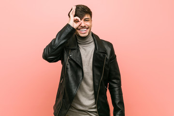 Fototapeta premium Young hispanic man wearing a leather jacket excited keeping ok gesture on eye.