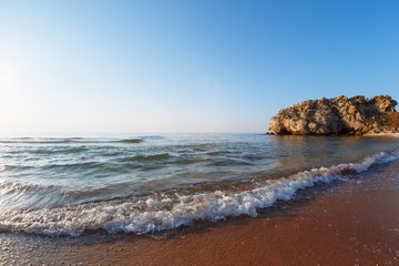 Sea with waves in a wild bay at sunset