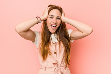 Fototapeta premium Young ginger woman with freckles laughs joyfully keeping hands on head. Happiness concept.