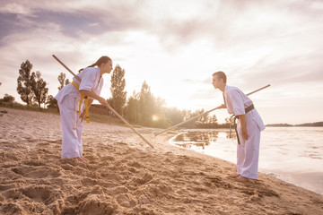 Two karate teenagers are training to fight in the sand against the background of the river