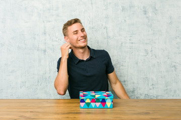 Fototapeta premium Young caucasian man holding a gift box on a table dancing and having fun.