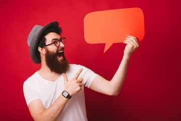 Photo of excited bearded guy, pointing at empty blank, over red isolated background