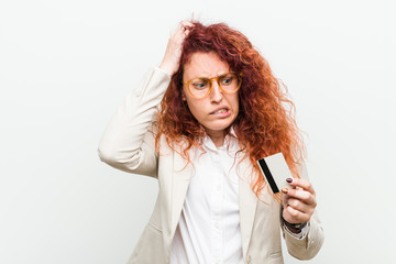 Young caucasian redhead woman holding a credit card being shocked, she has remembered important meeting.