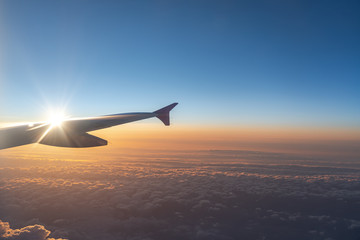 Fototapeta na wymiar Up in the air, view of aircraft wing silhouette with dark blue sky horizon and cloud background in sun rise time, viewed from airplane window