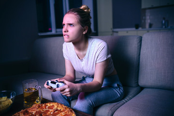 Young woman playing game at night. Sitting on sofa in dark room and look forward. Pizza on table....