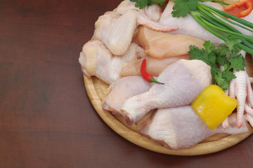 Assortment of diffeent chicken meat parts with vegetables on round cutting board on brown table