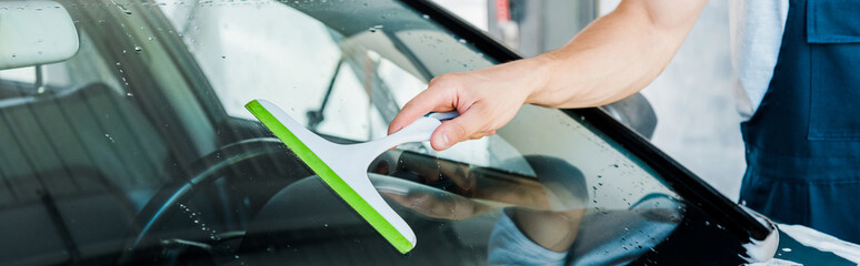 panoramic shot of car washer holding squeegee while cleaning car window