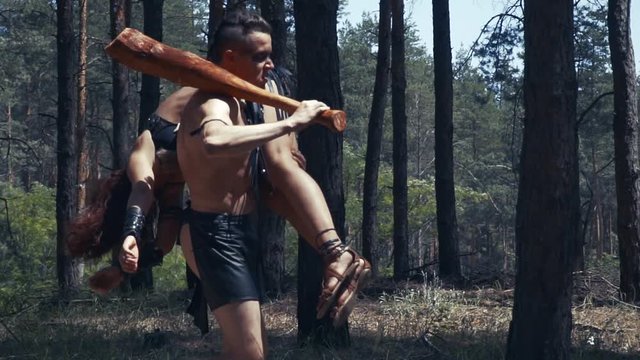 Barbarian is carrying an unconscious woman on his shoulder through the forest