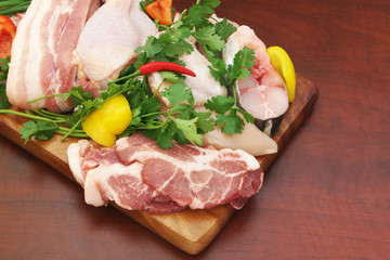 Pork, chicken and fish with vegetables and greens on  cutting board 