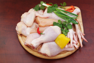 Assortment of diffeent chicken meat parts with vegetables on round cutting board