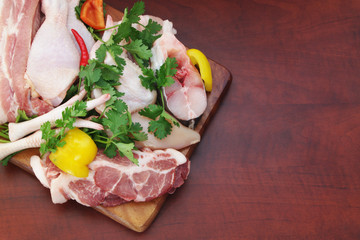 Assortment of pork, chicken and fish with vegetables and greens on wooden cutting board with room for text