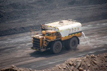 Big yellow truck spraying water in dusty Chinese coal mine