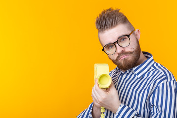 Fototapeta premium Unidentified young man with a yellow camera with a mustache and a beard on a yellow background. Concept photography and hobby.