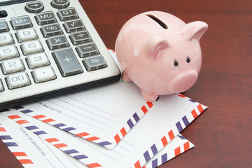 Calculator, piggy bank and mail envelopes on wooden table, saving money for delivery concept