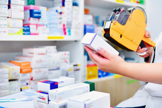 Hand Of The Pharmacist Using Yellow Labeling Gun For Sticking Price Label Of Medicine In Pharmacy Drugstore