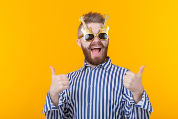 Joyful hipster young man raising his thumbs up in glasses with guitars posing against a yellow background. The concept of a successful party and holiday