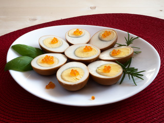 Pickled, marinated, egg halves decorated with caviar and greens on a white plate on a red mat,...