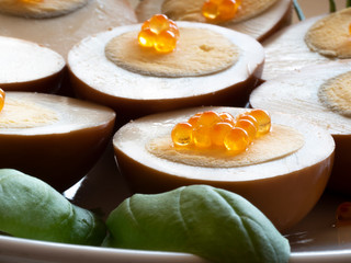 Pickled, marinated, egg halves decorated with caviar and greens on a white plate on a red mat, light table top, close up.
