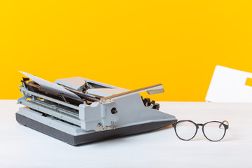 Workplace of the manager of the secretary and business typewriter and glasses are on the table on a yellow background. Office work concept.