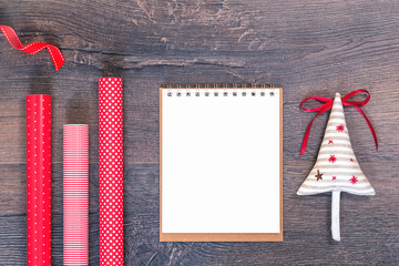 Handmade sewn Christmas tree and red striped and polka dot gift wrapping paper rolls and open notebook on wooden background. Festive New Year or season greetings card or banner flat lay copy space