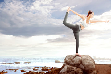 Asian healthy woman practicing yoga on the rock at beach