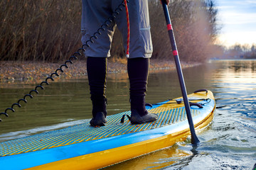 Men's legs on SUP (stand up paddle board) in water of the autumn river at sunset