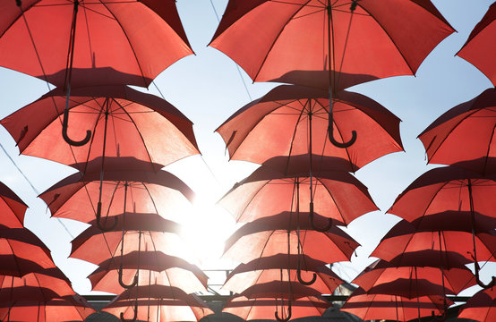 Red marsala umbrellas against the blue sky and sun. View from below. Abstract background with red umbrellas. Seamless pattern with umbrellas.