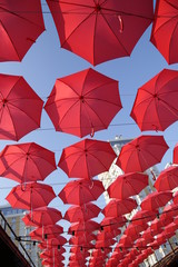 Fototapeta na wymiar Red umbrellas against the blue sky and the bright building. Abstract background with umbrellas