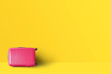 Pink suitcase standing next to the orange pastel color wall. Travel concept