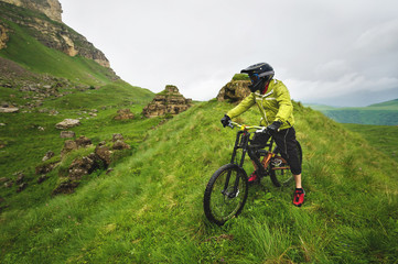 Fototapeta premium Side view of a man on a mountain bike standing on a rocky terrain and looking at a rock. The concept of a mountain bike and mtb downhill