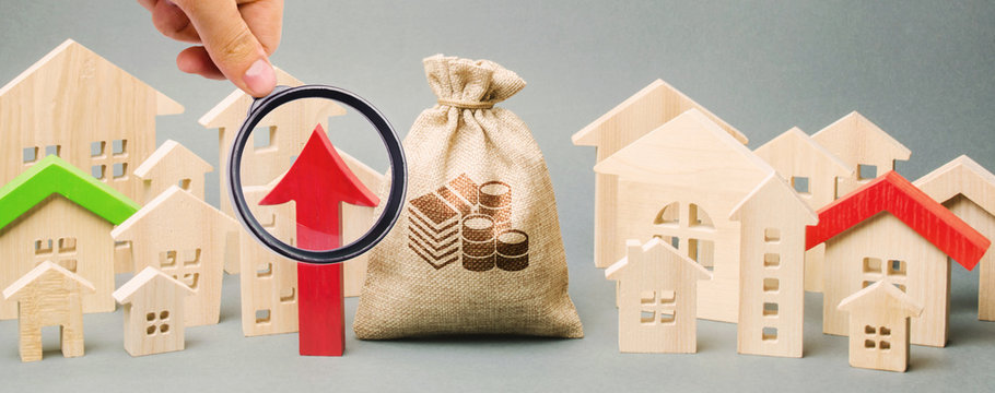 Red arrow up, money bag and miniature wooden houses. The concept of rising property prices. High mortgage rates. Expensive rental apartment. Growing demand for home purchase. Real estate market.