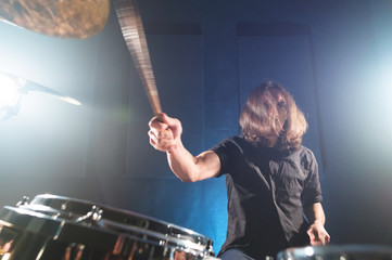 Fototapeta premium Portrait of a long-haired drummer with chopsticks in his hands sitting behind a drum set. Low key. Concepts of the creative freedom of the millenial generation
