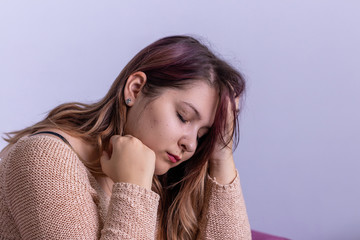 Fototapeta premium Sad depressed woman in living room sitting on couch, looking down and touching her forehead, loneliness and pain concept.