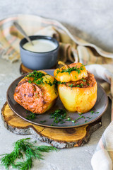 Baked bell peppers with filling. Minced rice, carrots in a plate on a wooden stand and a gray concrete background in a traditional rustic style.