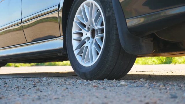 Detail view on wheel of powerful car starting movement and slipping on asphalt road. Small stones and dust flying out from under tire of auto. Vehicle beginning motion. Concept of burnout. Slow motion