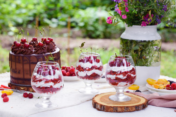 Gourmet picnic lunch in a park spread on a rug around a hamper with wine, cheese, fresh fruit, , bread rolls, cake, pickles and wraps on green spring grass under a tree
