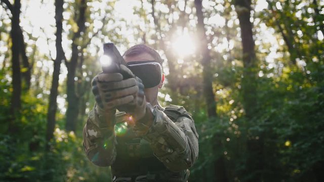 Soldier aiming with gun wearing virtual reality glasses outdoors