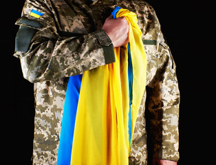Ukrainian soldier holds in his hand the yellow-blue flag of the state, he pressed his hand to his...